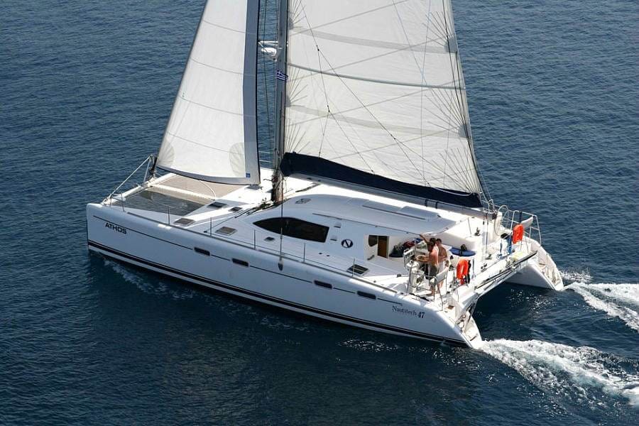 Catamaran under sail with mainsail and jib raised, guests visible on the deck, cruising in open water