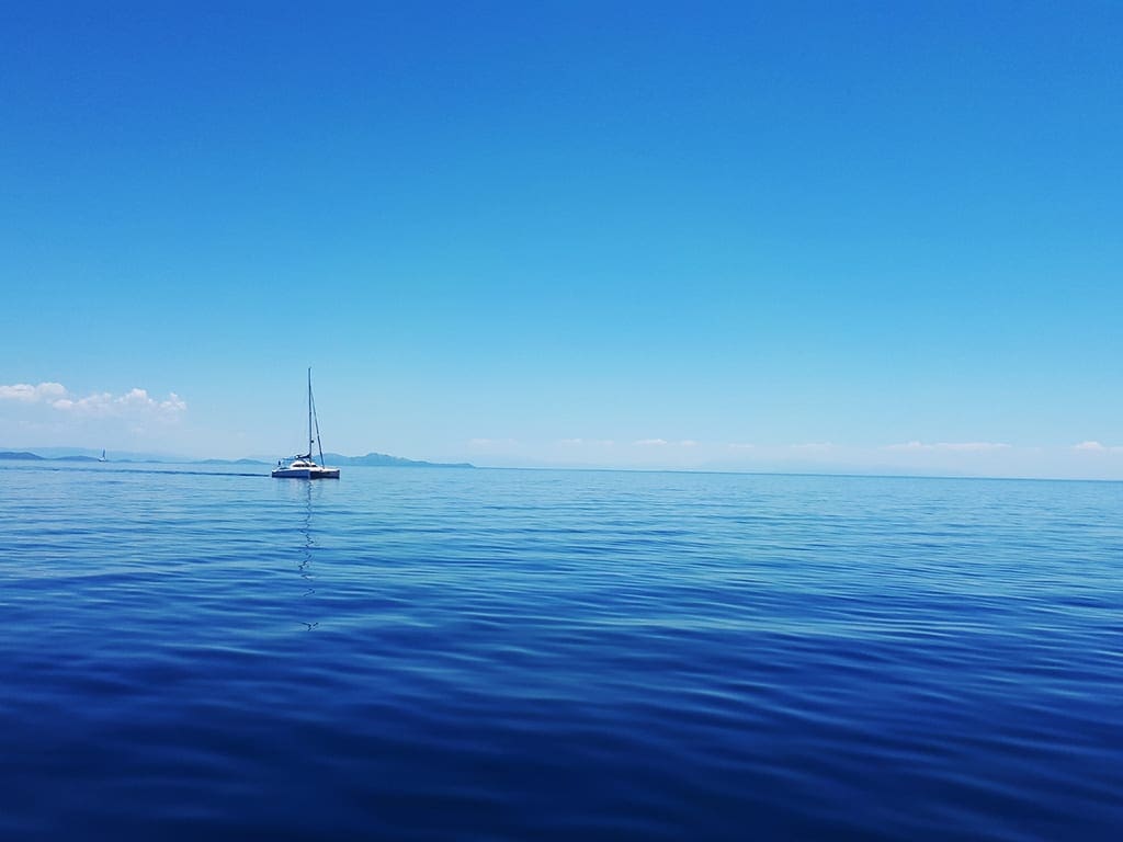 Catamaran at anchor in calm, clear blue waters with distant mountains on the horizon
