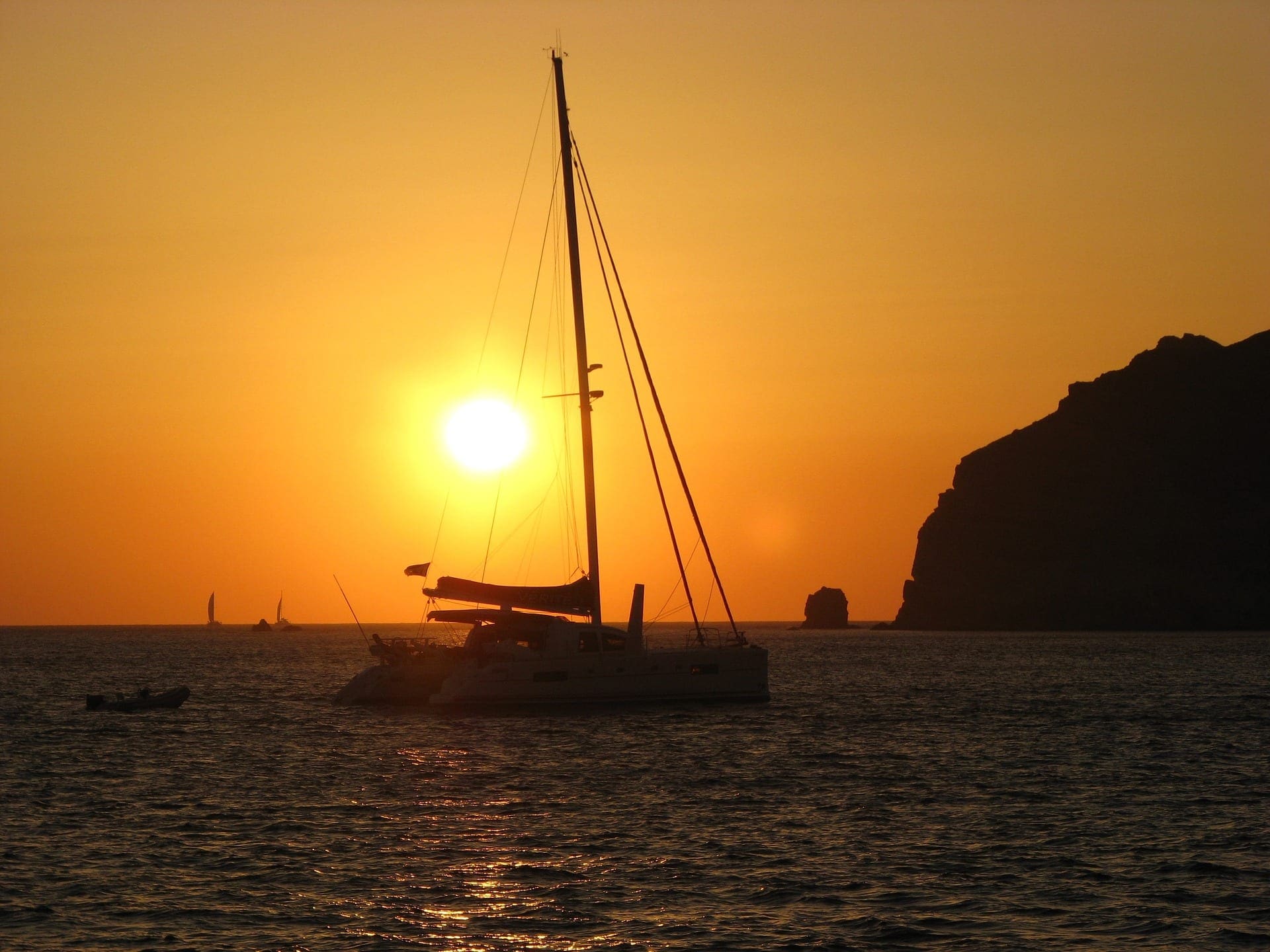 Catamaran anchored at sunset with rocky coastline silhouetted against golden sky and calm water