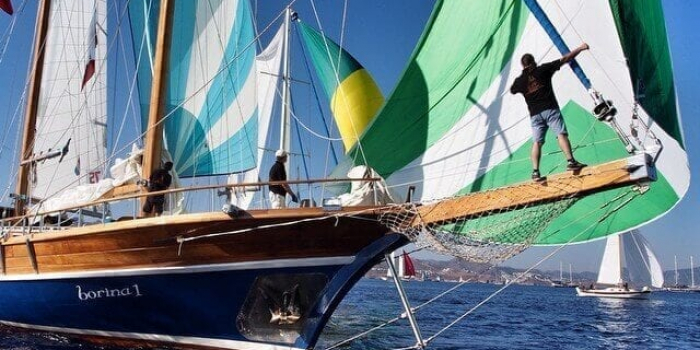 Man on the bow of a large sailing yacht with yachts in the back ground.
