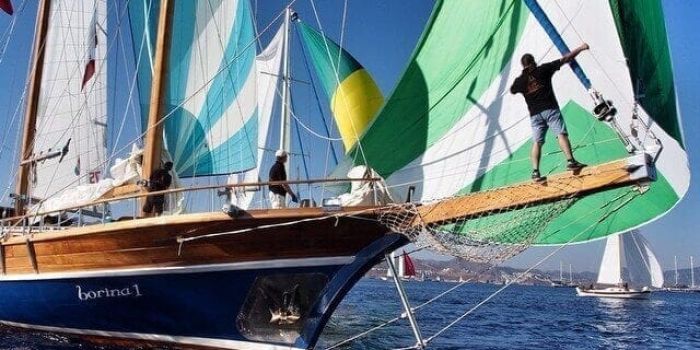 Man on the bow of a large sailing yacht with yachts in the back ground.